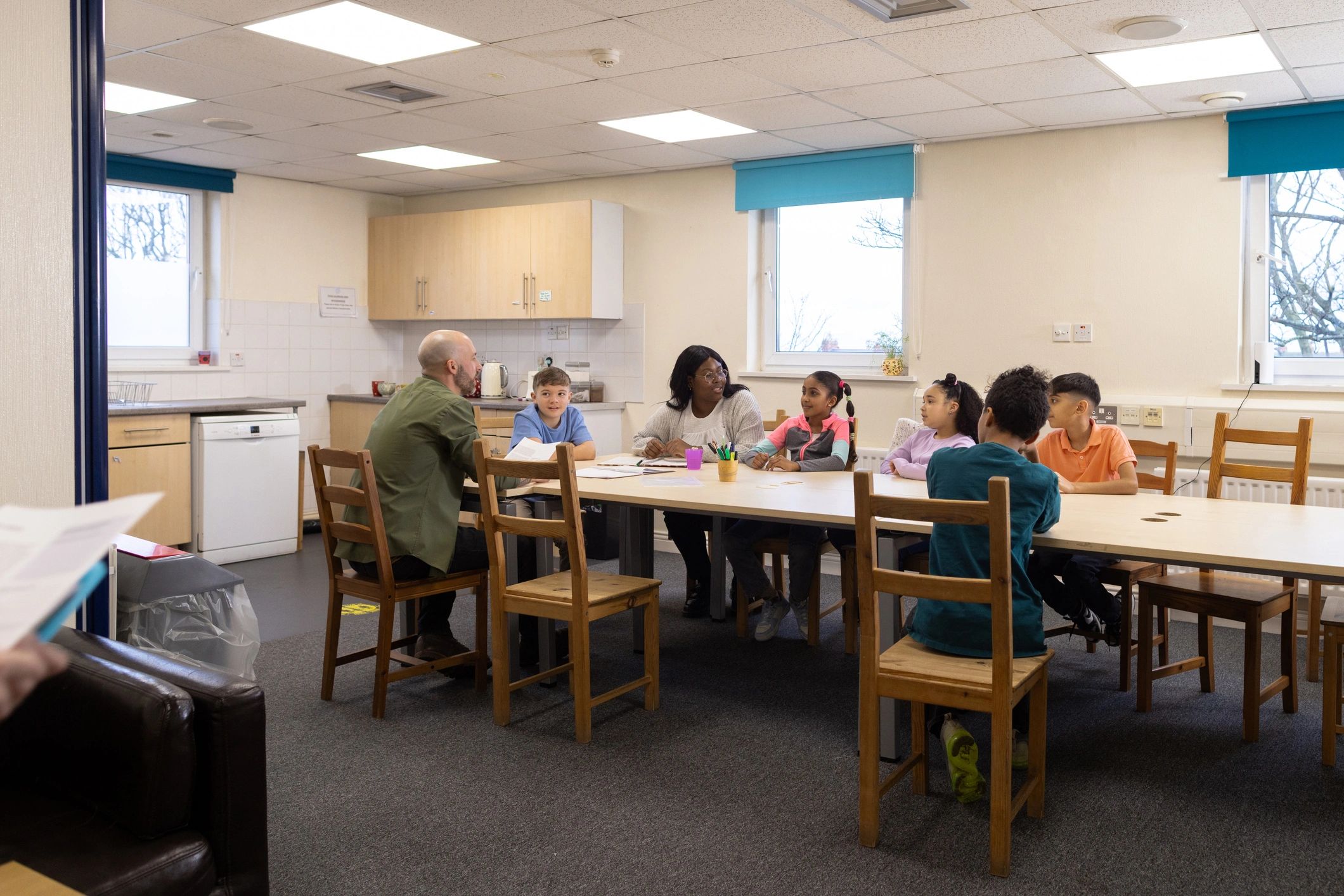 Children and adults gathered around a table in a supportive community setting